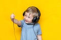 A smiling boy unplug his headphone and show plug to camera on isolated yellow background