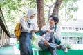 a smiling boy and veiled girl in Indonesian high school uniform chat under the tree while reading a book together