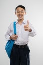 a smiling boy wearing a school uniform and carrying a backpack with thumbs up Royalty Free Stock Photo