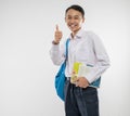 a smiling boy wears a school uniform and carries a backpack and book with thumbs up to the camera Royalty Free Stock Photo