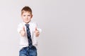 Smiling boy in white shirt and tie on grey wall background. Fashionable male child showing thumb up. Kids style fashion Royalty Free Stock Photo