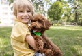 smiling boy of 6-7 years old sits on the grass with a fluffy brown poodle puppy