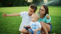 Smiling boys and girl sitting on green meadow. Kids taking selfie on smartphone Royalty Free Stock Photo