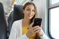 Smiling Brazilian businesswoman using smartphone social media app while commuting to work in train. Woman sitting in transport.