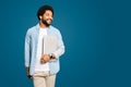 A smiling Brazilian young man, freelancer or student carrying a laptop standing isolated on blue