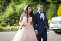 Smiling bride with a bouquet and happy groom walking to the wedding aisle car in the background Royalty Free Stock Photo