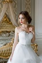 Smiling bride with chic makeup and hairstyle in a white wedding dress is standing in a bedroom Royalty Free Stock Photo