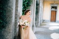 Smiling bride in a dress with a bouquet of pink flowers sat down near a pillar in a vaulted room. Lake Como Royalty Free Stock Photo