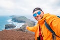 Smiling brightly dressed backpacker man taking selfie portrait as he hiking and enjoying Atlantic ocean view on Ponta de Sao