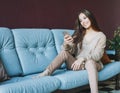 Smiling brunette asian young woman in casual using mobile sitting on sofa at home