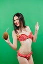 Smiling Brunette in Bright Swimsuit with Tropical Cocktail in Hands Posing in Studio on Green Background. Royalty Free Stock Photo