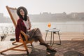 Smiling brunette girl sitting on recliner enjoying vacation in Europe. Portrait of well-dressed lady in good mood