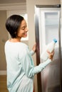 Smiling brunette holding milk bottle with open refrigerator Royalty Free Stock Photo