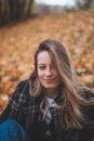 Smiling brunette sitting in a pile of colorful leaves in an oak forest. Candid portrait of a young realistic woman in autumn