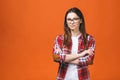 Smiling brunette woman in eyeglasses and casual posing with crossed arms and looking at the camera over orange background Royalty Free Stock Photo