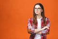Smiling brunette woman in eyeglasses and casual posing with crossed arms and looking at the camera over orange background Royalty Free Stock Photo