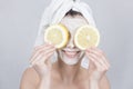 Smiling brunette woman holding two slice of lemon in front of her face. woman with moisturizing facial mask