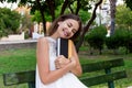 Smiling brunette woman is hugging her favourite book on the bench in the park