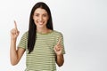 Smiling brunette woman pointing fingers at two ways, showing variants, standing in t-shirt over white background Royalty Free Stock Photo