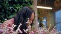 Smiling brunette woman sniffing small pink flowers indoors