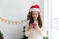 Smiling brunette woman in sweater and SantaÃ¢â¬â¢s hat holding small gift box and rejoices over Christmas decorative Royalty Free Stock Photo