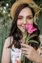 Smiling brunnete happy girl in a white-flowers dress and hat with pink peones. Sun is on the background