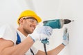 Smiling builder in hardhat drilling wall indoors