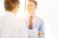 Smiling business colleagues discussing over document by wall at office with yellow lens flare in background