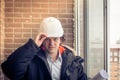 Smiling business engineer with white safety helmet holding blueprint project plan on brick building background, happy Royalty Free Stock Photo