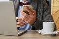 young businessman sitting at a table in a cafe with a laptop and a cup of coffee using a smartphone