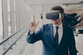 Smiling business professional in suit wearing VR headset on head using virtual reality at workplace Royalty Free Stock Photo