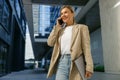 Smiling business woman holding laptop and talking phone standing on modern building background Royalty Free Stock Photo