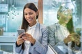 Business woman leaning on glass with her reflection and scrolling social media networks during short break in office. Royalty Free Stock Photo