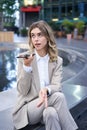 Smiling business woman record voice message, speaking into microphone on mobile phone, sitting near fountain on street Royalty Free Stock Photo