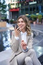 Smiling business woman record voice message, speaking into microphone on mobile phone, sitting near fountain on street Royalty Free Stock Photo