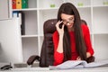 Smiling business woman in red dress sitting and writing something by the table as well as looking at camera