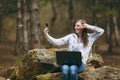 Smiling business woman or student sitting on stone with laptop doing selfie and showing victory sign on mobile phone in Royalty Free Stock Photo