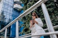 Smiling business woman in white suit and sunglasses using phone during break standing near modern office building Royalty Free Stock Photo