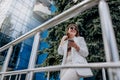 Smiling business woman in white suit and sunglasses using phone during break standing near modern office building Royalty Free Stock Photo