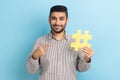 Smiling businessman with beard pointing at large yellow hash symbol, wearing striped shirt.