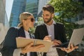 Man and woman in classic suit discussing business details and using laptop while standing outdoors Royalty Free Stock Photo