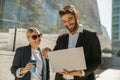 Man and woman in classic suit discussing business details and using laptop while standing outdoors Royalty Free Stock Photo