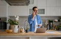 Smiling businessman discussing over smart phone while working over laptop at kitchen counter at home Royalty Free Stock Photo