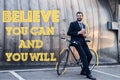 smiling businessman with disposable cup of coffee leaning on bicycle on street with believe you can