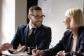 Smiling businessman in eyeglasses talking to middle aged female partner.