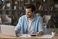 Smiling businessman in glasses using laptop, calculating bills, managing finances