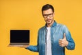 Smiling businessman holding blank laptop screen isolated over yellow background. Looking at camera. Royalty Free Stock Photo
