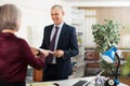 Smiling businessman holding out papers to woman in office Royalty Free Stock Photo