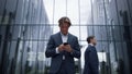 Smiling businessman holding smartphone at modern office building. Downtown area Royalty Free Stock Photo