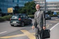 Smiling businessman with laptop bag waiting for taxi cab in the city during sunny day Royalty Free Stock Photo